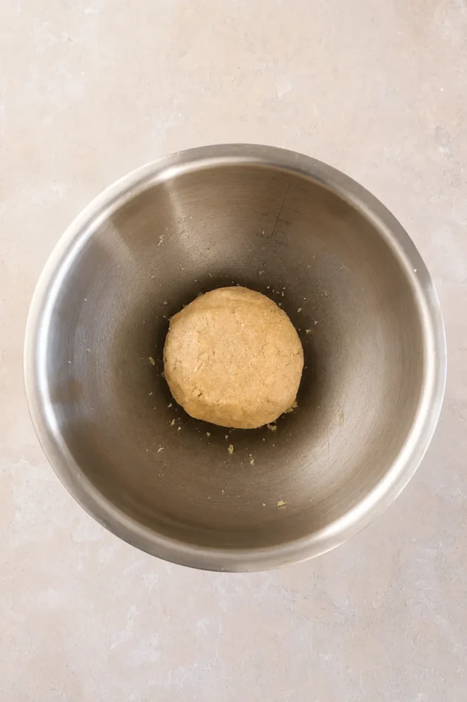 Ball of gluten-free vegan tart dough resting in a stainless steel bowl, ready to be chilled before shaping.
