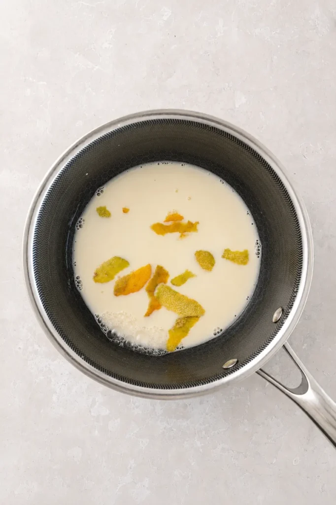 Saucepan with plant milk and lemon peel, used to prepare the filling for a vegan lemon curd tart.