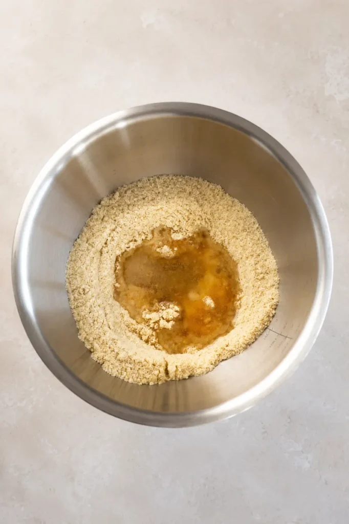 Top-down view of almond flour mixture with maple syrup and coconut oil in a stainless steel bowl, ready to be mixed for a gluten-free vegan tart crust.