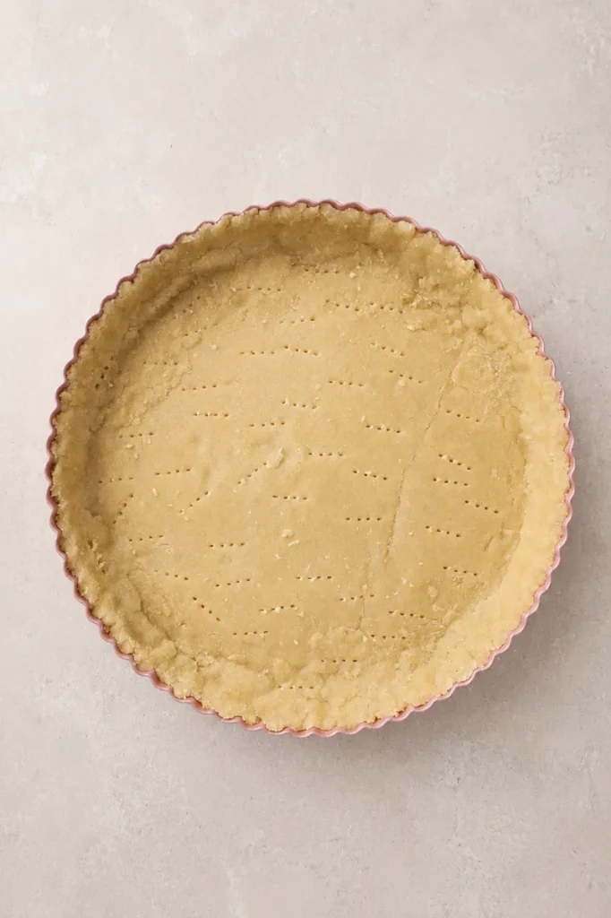 Top-down view of a gluten-free tart crust pressed into a fluted tart pan and pricked with a fork before baking.