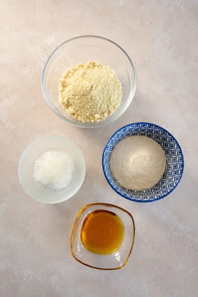 Top-down view of almond flour, brown rice flour, coconut oil and maple syrup measured for a gluten-free vegan tart crust.