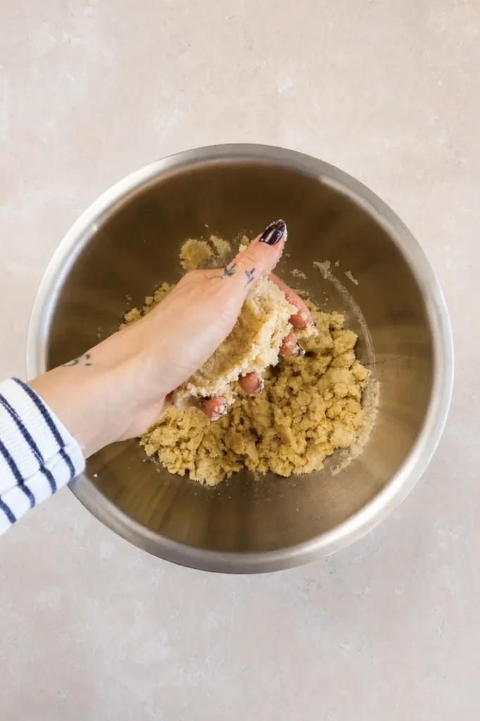 Hand pressing gluten-free tart dough in a stainless steel bowl to check that the mixture holds together.