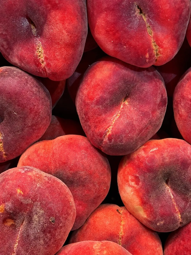 Vegan Mediterranean diet seasonal flat peaches with natural imperfections, photographed in a close-up market display.