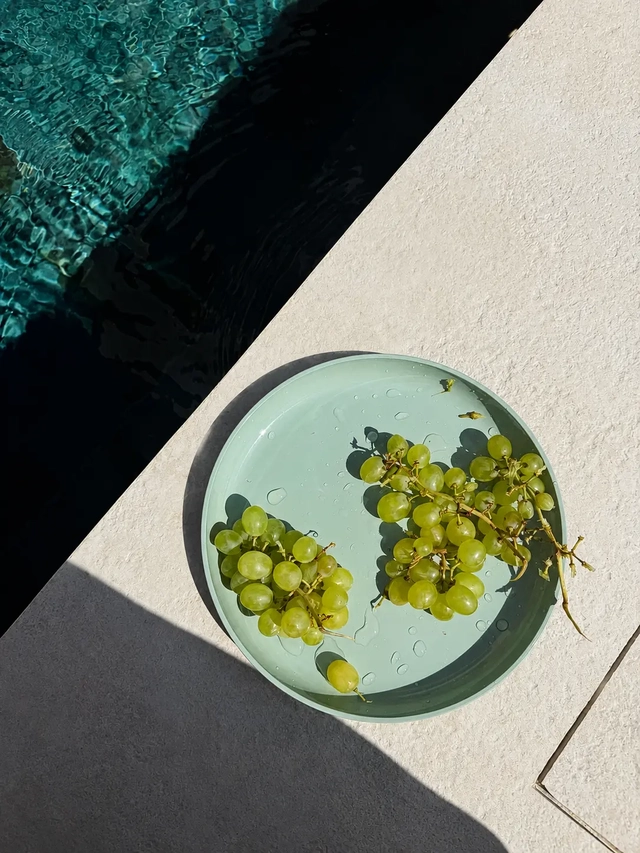 Vegan Mediterranean diet fresh green grapes on a pale plate beside a swimming pool in bright natural sunlight.