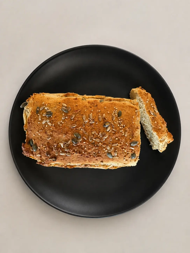 Vegan Mediterranean diet gluten-free seeded bread loaf served on a black plate with a sliced piece on the side.