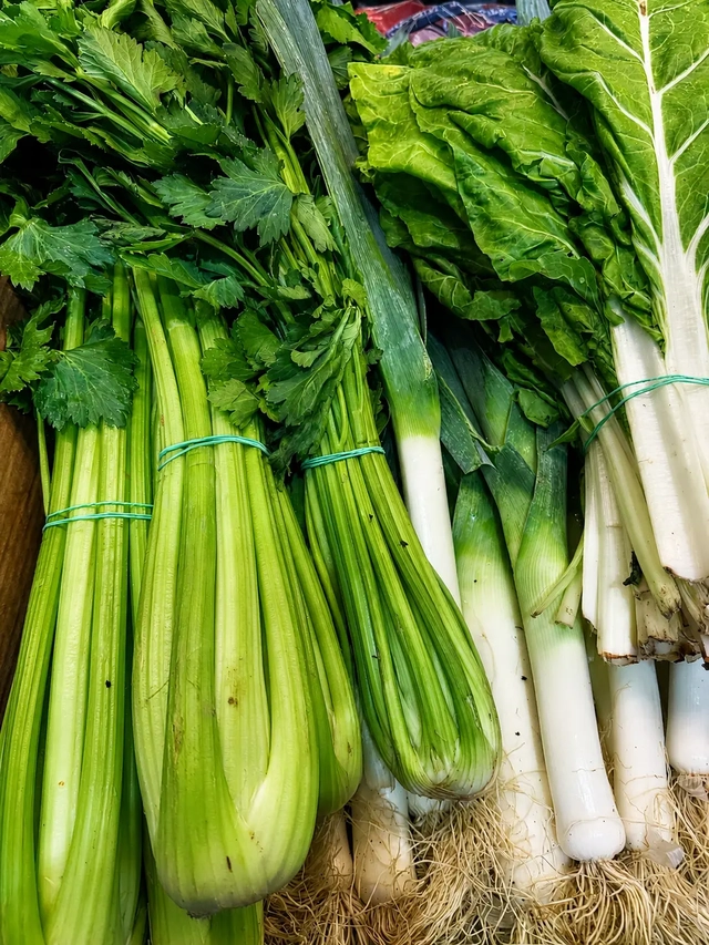 Vegan Mediterranean diet vegetables including celery, leeks, and leafy greens displayed fresh at a local market.