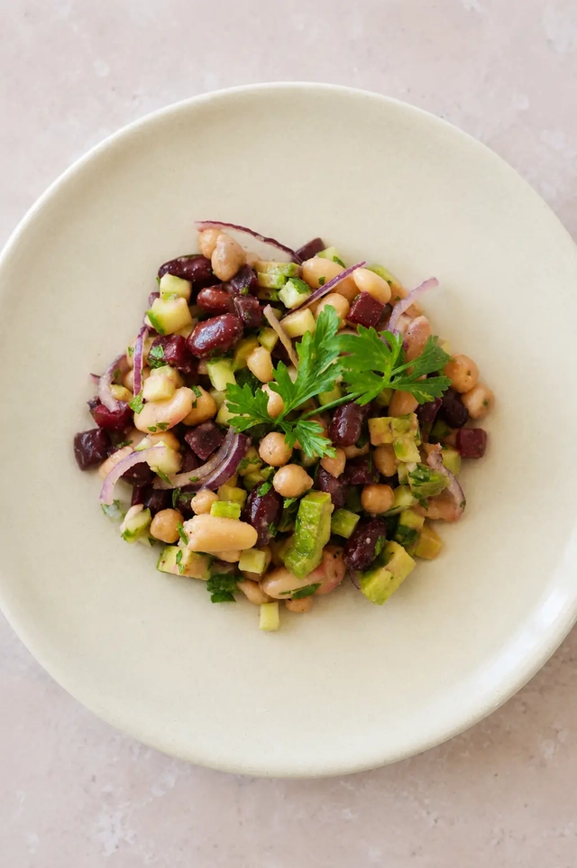 What I eat in a day as a vegan lunch with a mixed bean salad, chickpeas, kidney beans, cucumber, avocado, red onion, and parsley.