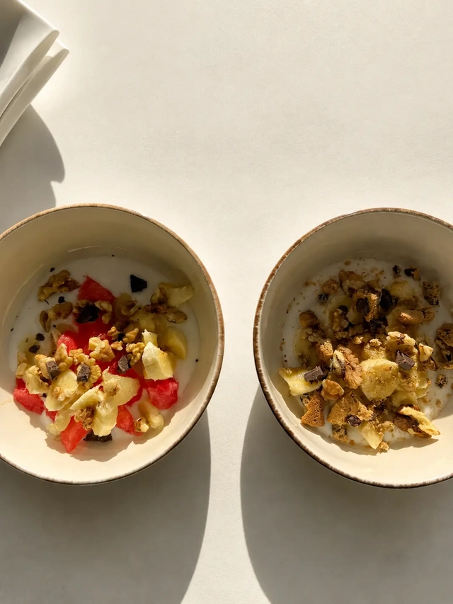 What I eat in a day as a vegan breakfast with plant-based yogurt bowls topped with fresh fruit, walnuts, granola, and dark chocolate.