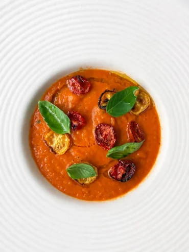 Creamy 3-ingredient tomato soup served in a white textured bowl, topped with roasted cherry tomatoes, fresh basil leaves and a drizzle of olive oil.