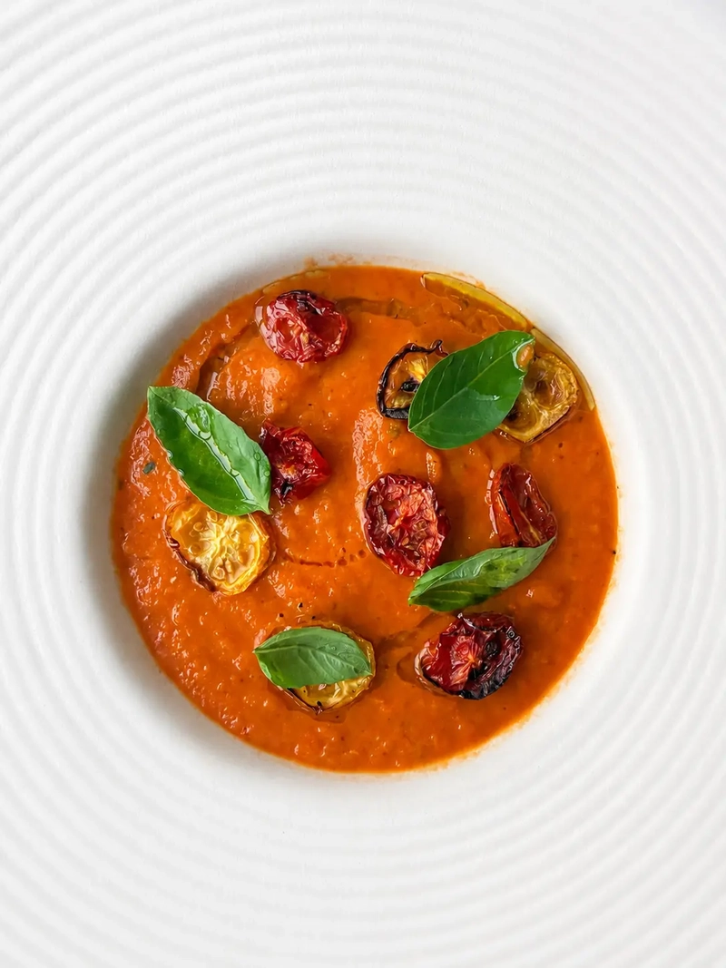 Creamy 3-ingredient tomato soup served in a white textured bowl, topped with roasted cherry tomatoes, fresh basil leaves and a drizzle of olive oil.