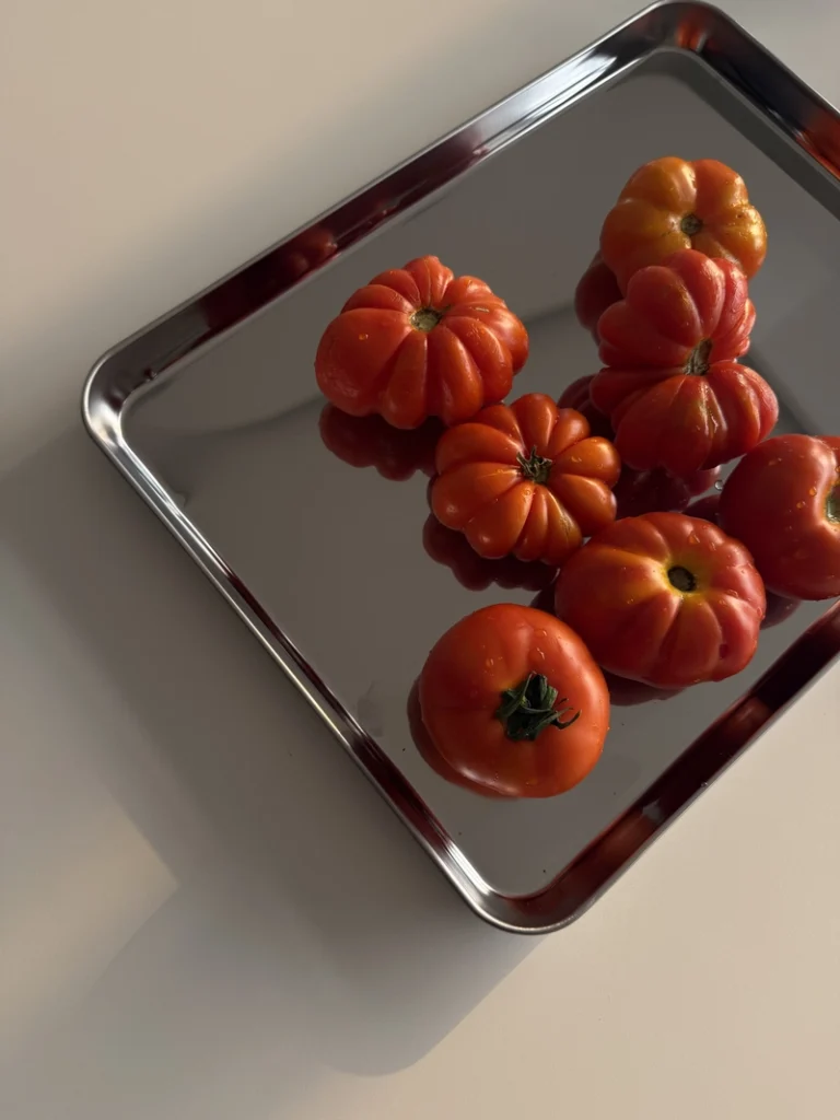 Fresh heirloom tomatoes arranged on a reflective metal tray in warm natural light, ready to be roasted for an easy 3-ingredient tomato soup.
