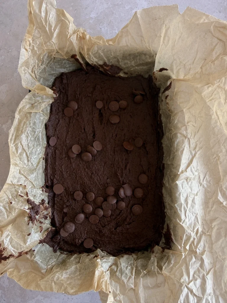 Ready to be baked high-protein vegan bean brownies topped with chocolate chips in a parchment-lined loaf pan.