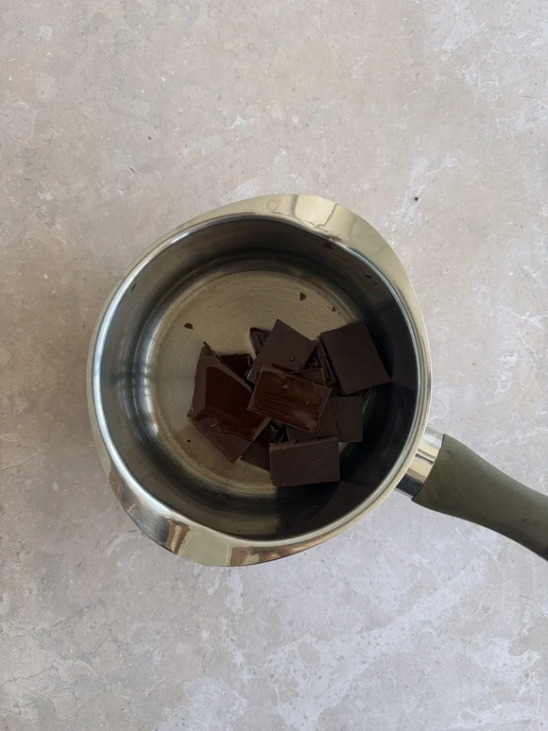 Dark chocolate pieces melting with coconut oil in a saucepan for high-protein vegan bean brownies.