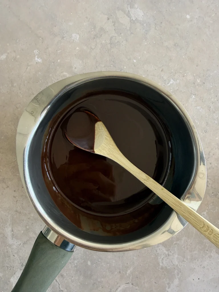 Smooth melted dark chocolate stirred with a wooden spoon for high-protein vegan bean brownies.
