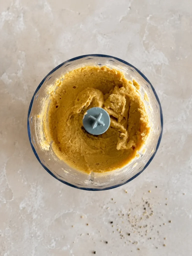 Chickpea purée blended until creamy in a food processor on a pale stone surface.