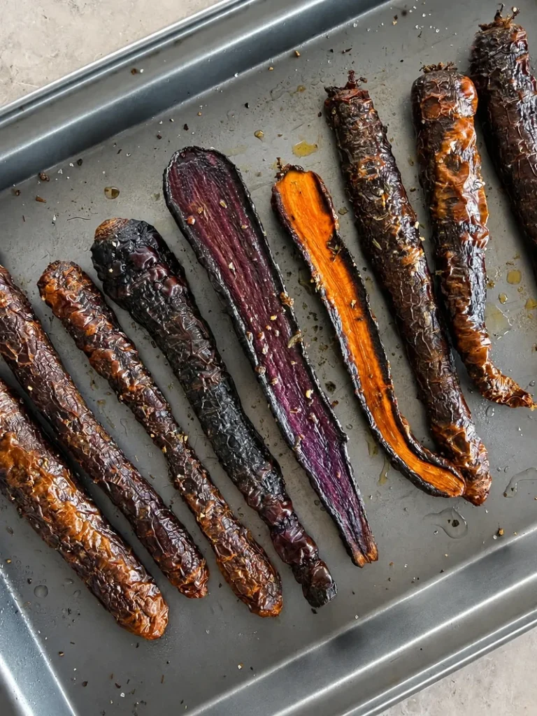 Roasted purple carrots on a baking tray, coated with oil and herbs, ready to be served after oven roasting.