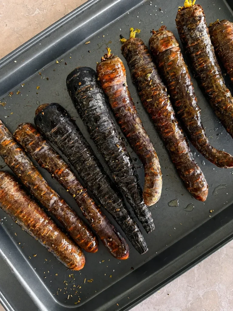 Roasted purple carrots on a baking tray, coated with oil and herbs, ready to be served after oven roasting.