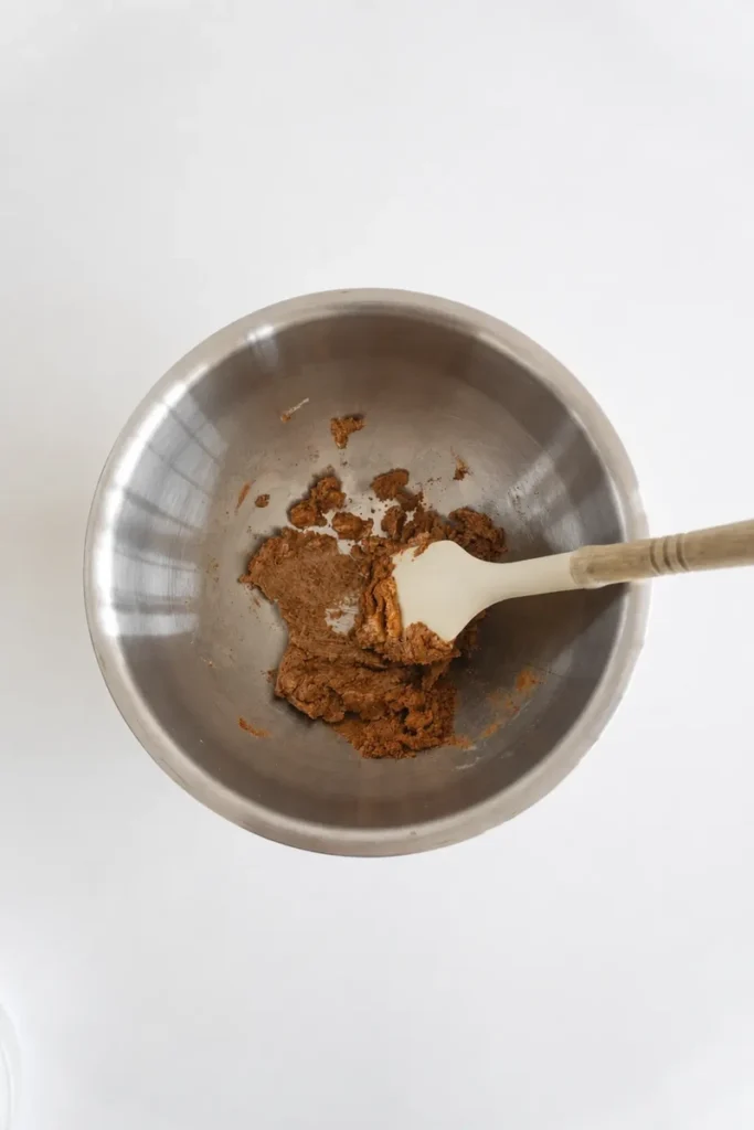 Coconut sugar and vegan butter creamed together in a mixing bowl for chocolate chip cookies without eggs, with a spatula mixing the dough.