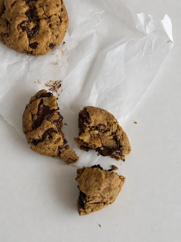 Vegan gluten-free chocolate chip cookies without eggs, broken into pieces to show the soft center and melted dark chocolate chunks.