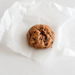 Single chocolate chip cookie without eggs on crumpled parchment paper, with a thick soft texture and visible dark chocolate chunks.