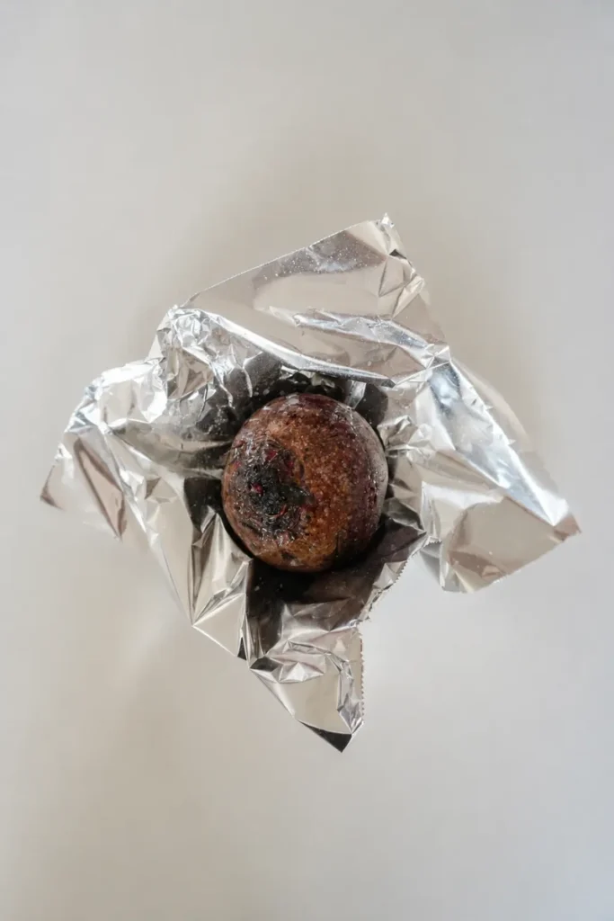 Whole beetroot resting in opened foil on a light neutral surface, ready to be cooked for the fig carpaccio.