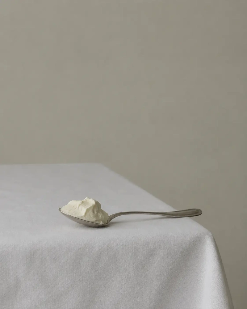 A silver spoon filled with soft cheese on a white linen tablecloth, illustrating the difference between vegan and dairy-free foods.