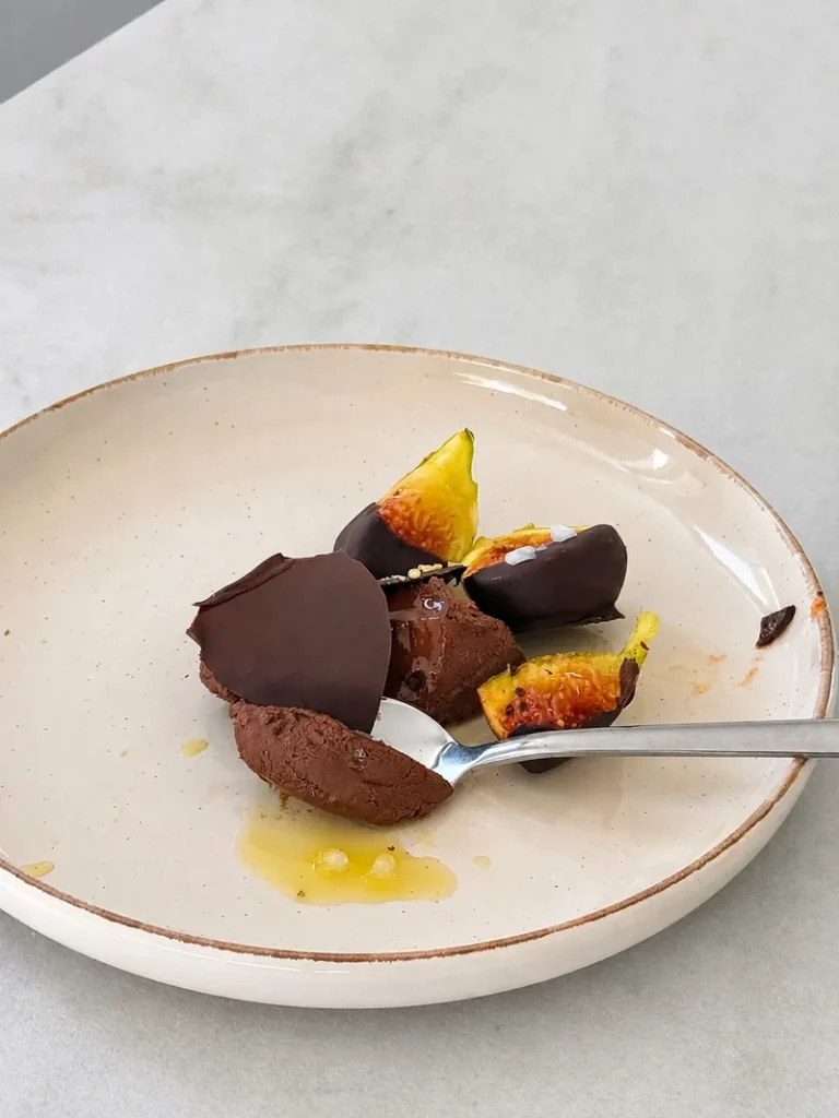 Chocolate mousse served on a cream ceramic plate with fresh figs, dark chocolate shards and a spoon, styled in soft natural light.