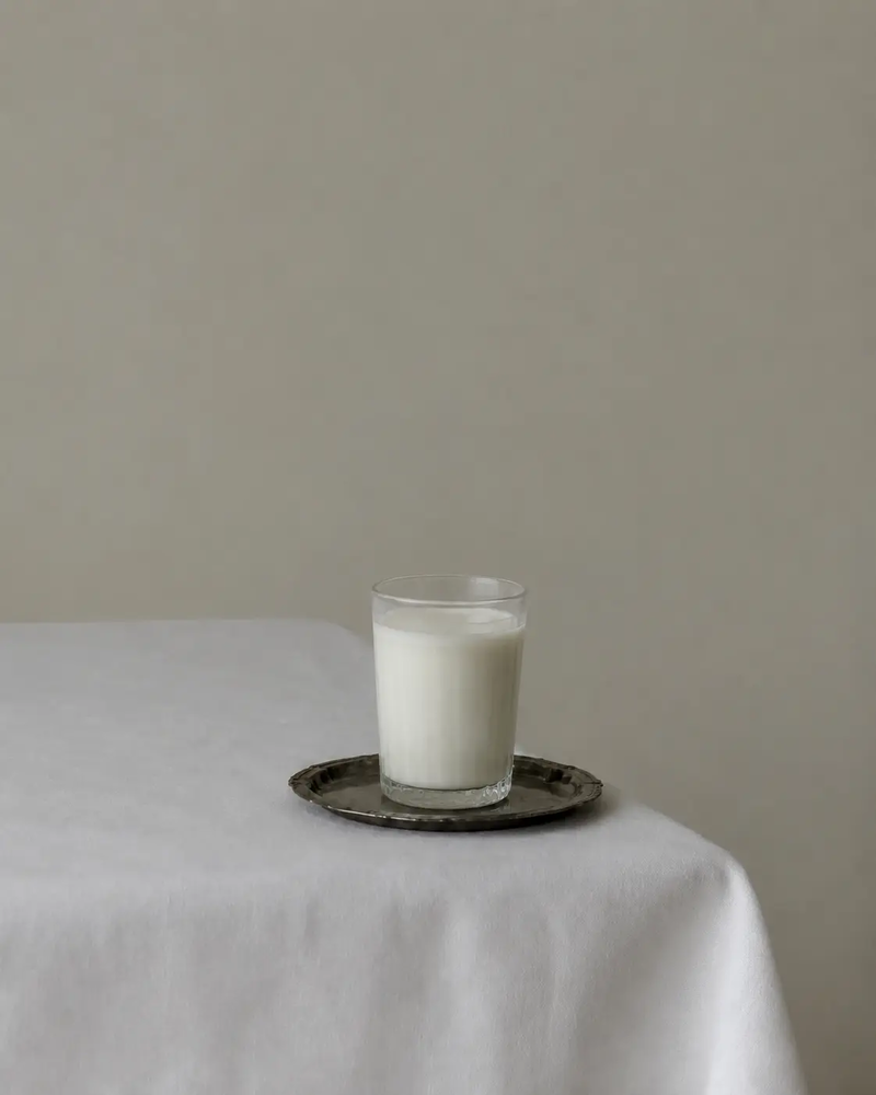 A glass of milk on a small antique tray illustrating the difference between vegan and dairy-free eating, styled on a white tablecloth against a neutral background.