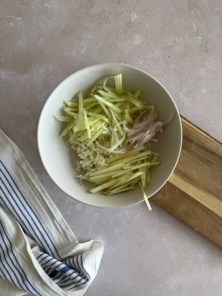Kachumber salad ingredients layered in a bowl with cucumber, cabbage, red onion and julienned green apple.