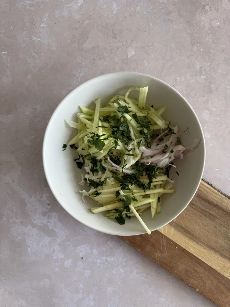 Kachumber salad ingredients layered in a bowl with cucumber, cabbage, red onion and julienned green apple.