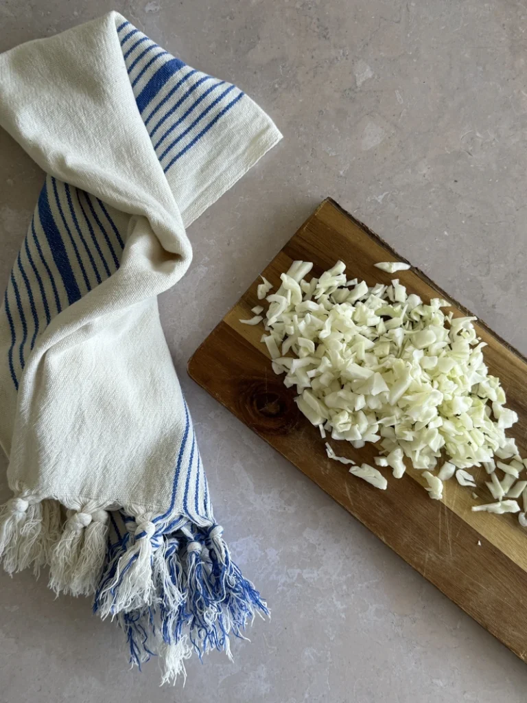Chopped cabbage on a wooden cutting board, prepared as an ingredient for kachumber salad, beside a blue-and-white striped kitchen towel.