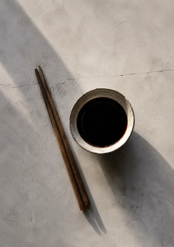 Tamari in a ceramic bowl with wooden chopsticks on a light stone surface, styled with soft natural shadows and a minimalist aesthetic.