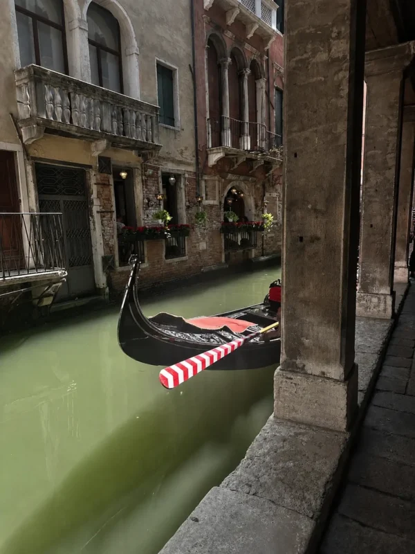 Black gondola on a narrow canal in Venice, Italy, framed by historic Venetian buildings and a shaded stone arcade.