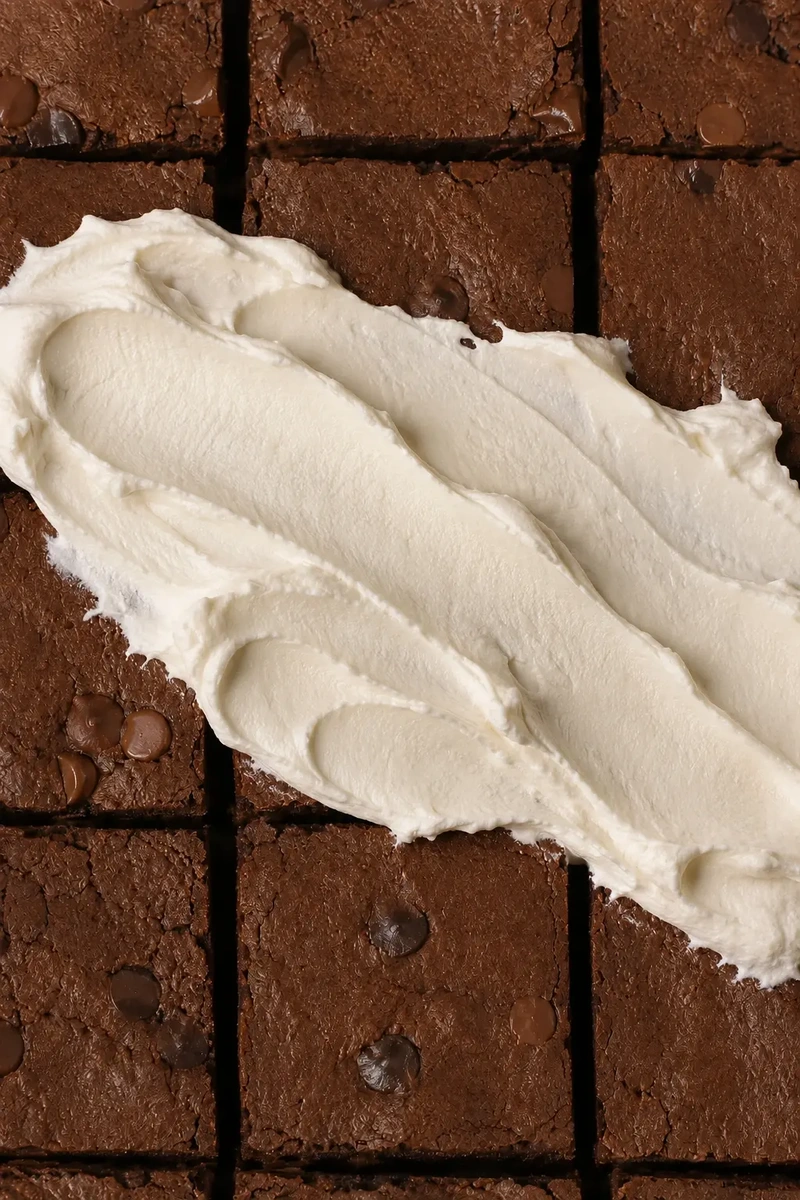 Close-up of high-protein vegan bean brownies topped with a generous swirl of whipped vegan cream and scattered chocolate chips.