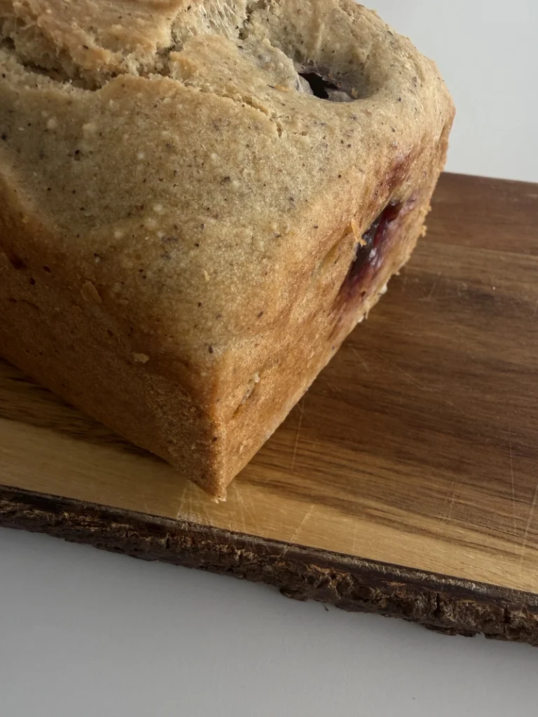 Close-up of vegan gluten-free fig bread with fresh figs on a rustic wooden board, showing the golden baked crust and whole fig baked through the loaf.