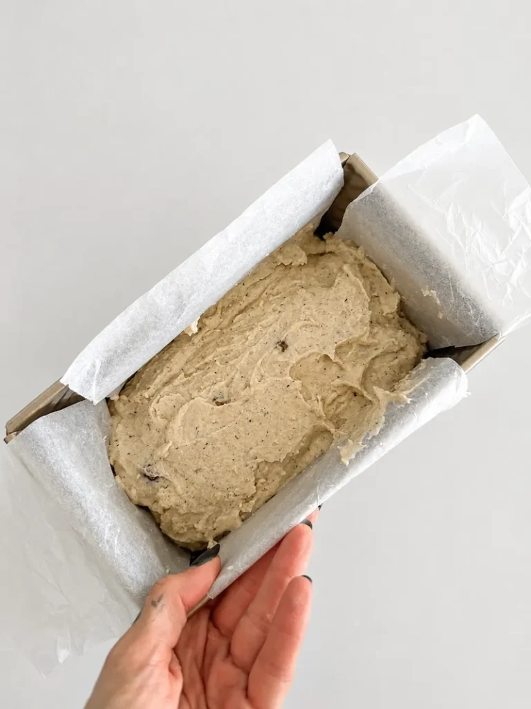 Gluten-free batter for vegan fig bread with fresh figs spread inside a parchment-lined loaf pan, ready for the whole figs to be added.
