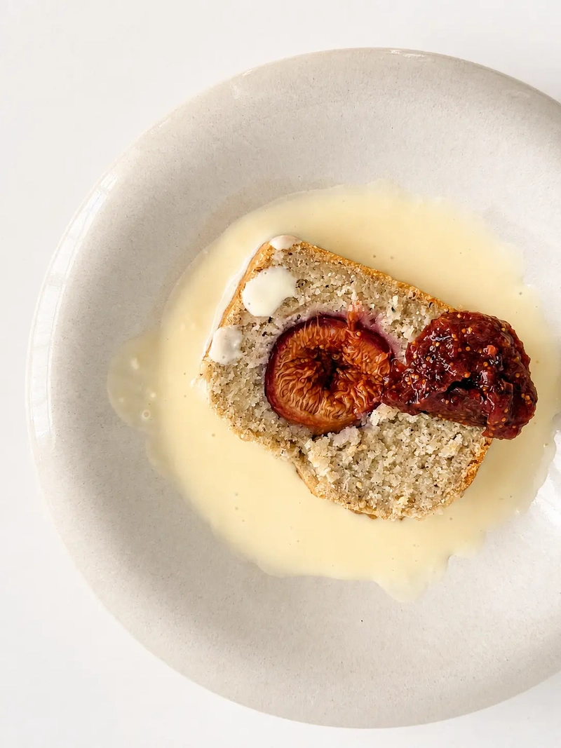 Overhead view of a slice of vegan gluten-free fig bread with fresh figs served on a plate with creamy vegan crème anglaise and a roasted fig on top.