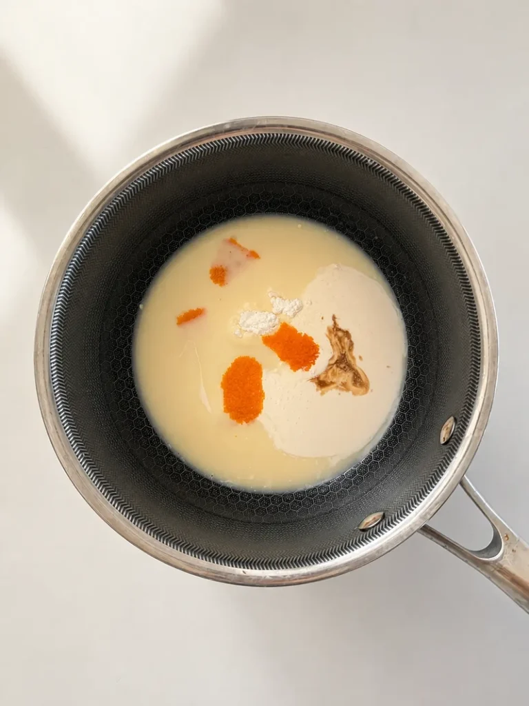 Overhead view of vegan crème anglaise ingredients in a saucepan, including soy milk, plant cream, orange zest, vanilla, and cornstarch before cooking.
