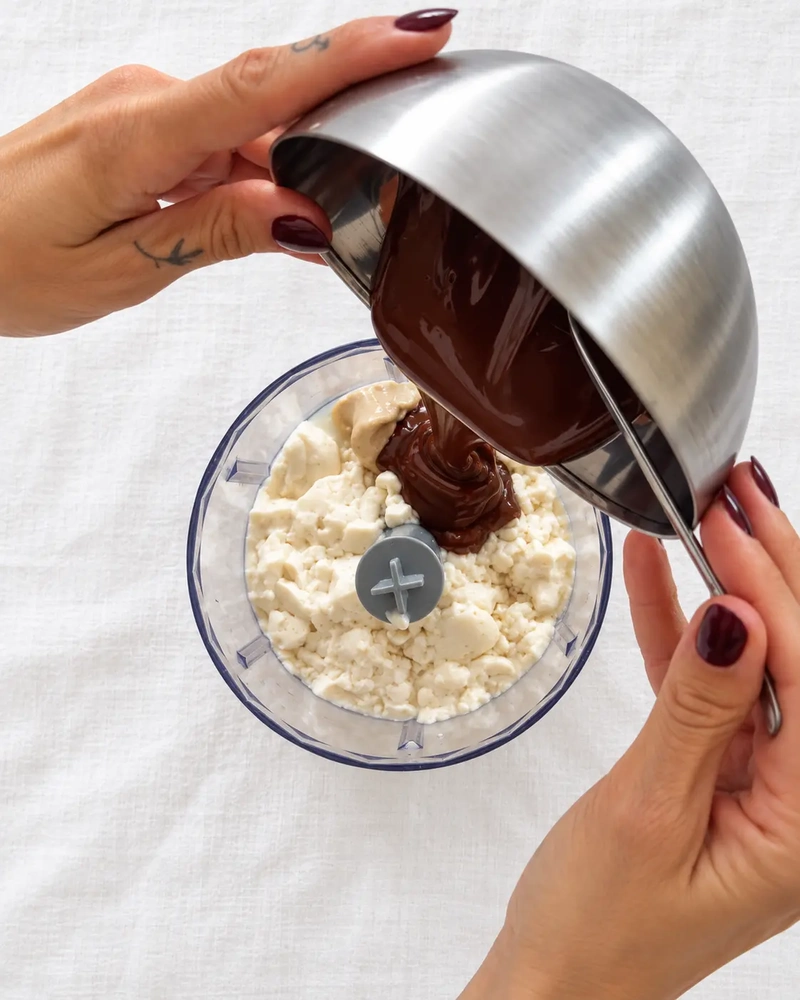 Melted dark chocolate being poured into a small food processor with silken tofu for tofu chocolate pudding.