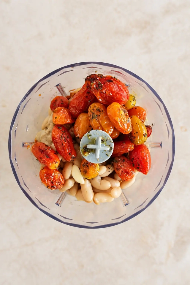 Roasted cherry tomatoes, white beans, garlic and seasonings in a blender, ready to make the creamy white bean base for vegan eggplant schnitzel.