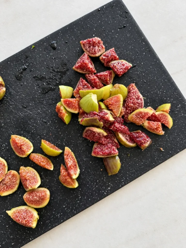 Chopped fresh figs on a black cutting board, with some pieces cut into wedges for garnish and others diced to cook into a creamy vegan fig risotto.