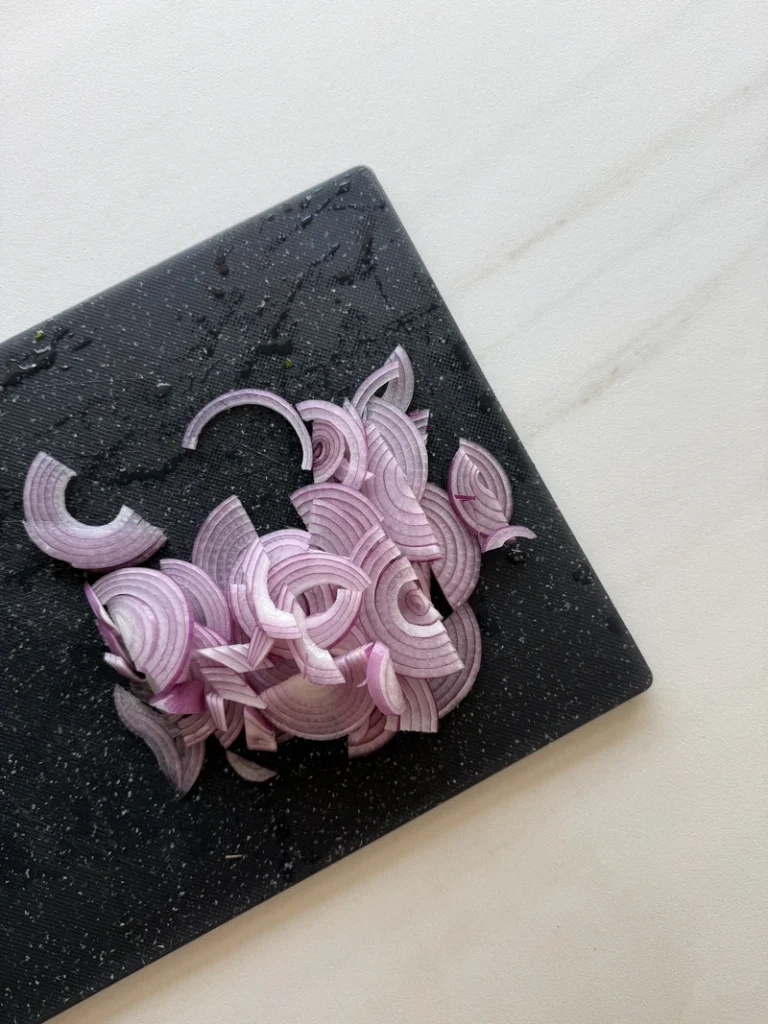Thinly sliced red onions arranged on a black cutting board, ready to be slowly caramelized for vegan fig risotto.