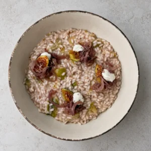 Creamy vegan fig risotto topped with caramelized red onions, fresh fig wedges and whipped vegan feta, served in a rustic ceramic bowl.
