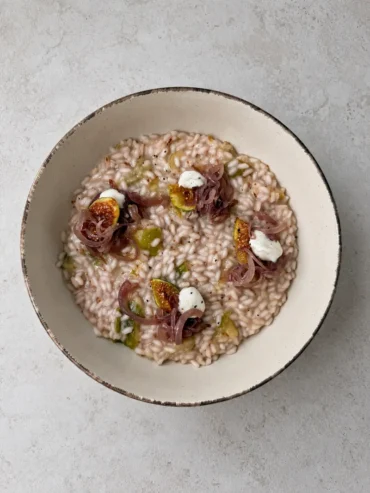 Creamy vegan fig risotto topped with caramelized red onions, fresh fig wedges and whipped vegan feta, served in a rustic ceramic bowl.