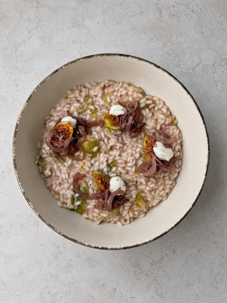 Creamy vegan fig risotto topped with caramelized red onions, fresh fig wedges and whipped vegan feta, served in a rustic ceramic bowl.