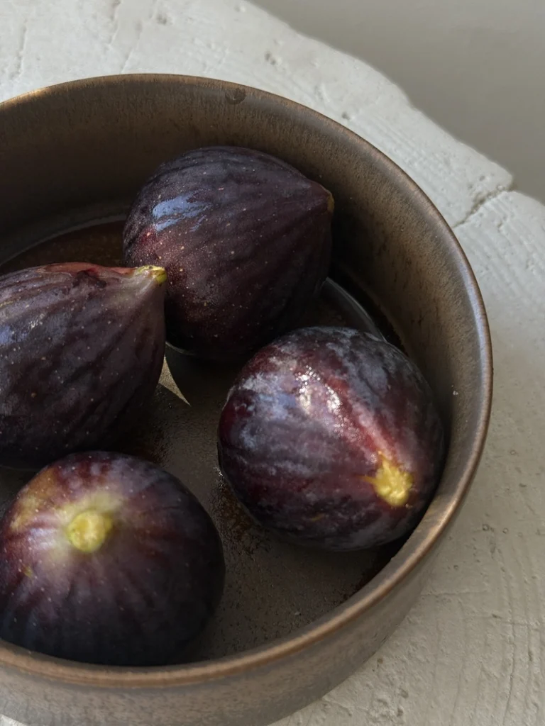 Four fresh, ripe dark purple figs in a rustic ceramic bowl, ready to be used in a creamy vegan fig risotto with caramelized onions.