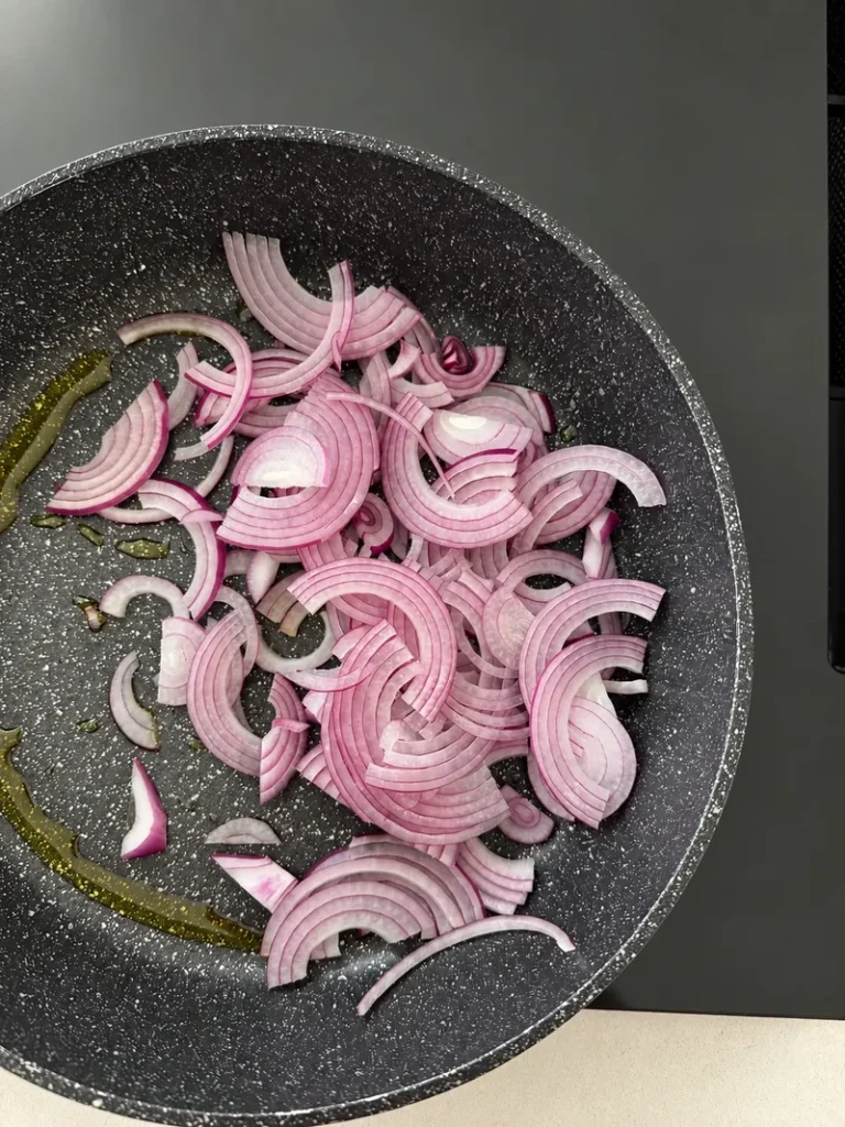 Thinly sliced red onions in a nonstick frying pan, ready to be slowly caramelized for vegan fig risotto.