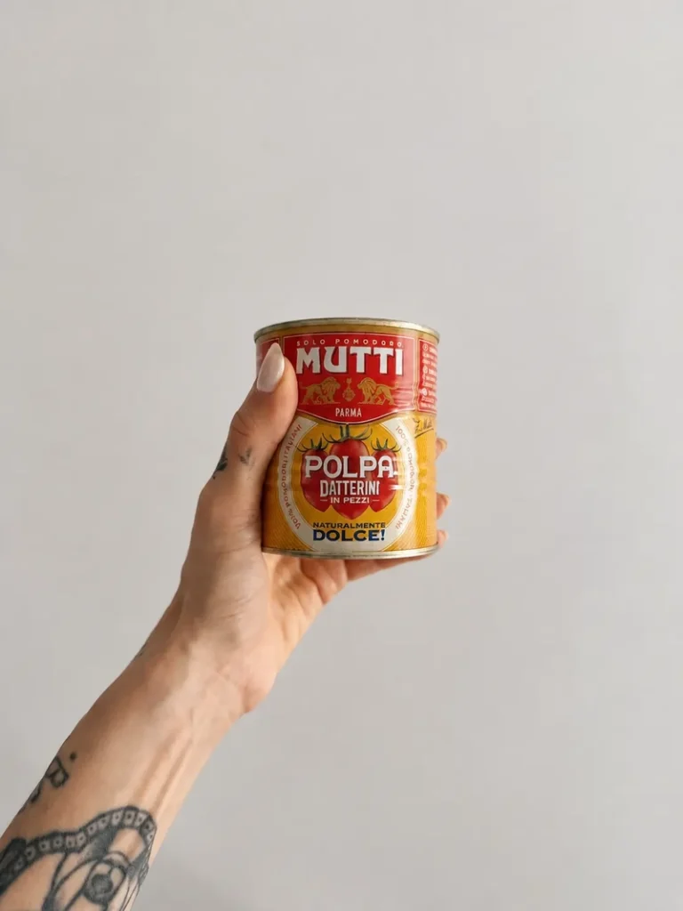 Hand holding a can of chopped tomatoes used to add extra umami to French onion soup with lentils.