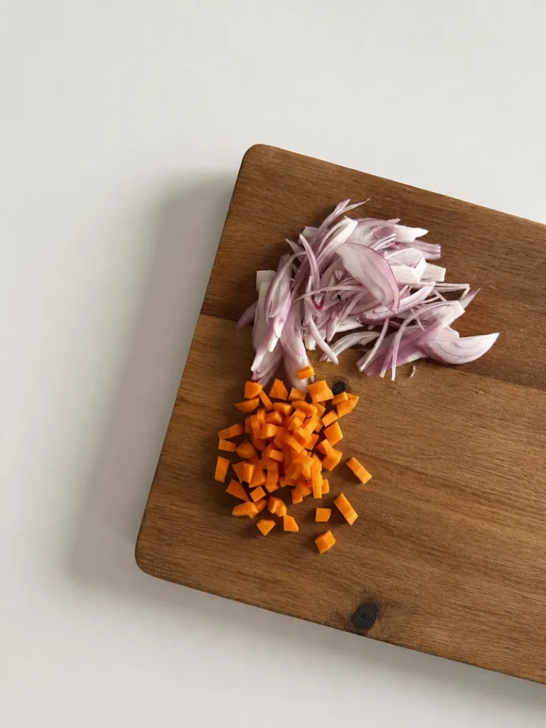 Thinly sliced onions and diced carrots prepared on a wooden cutting board for French onion soup with lentils.