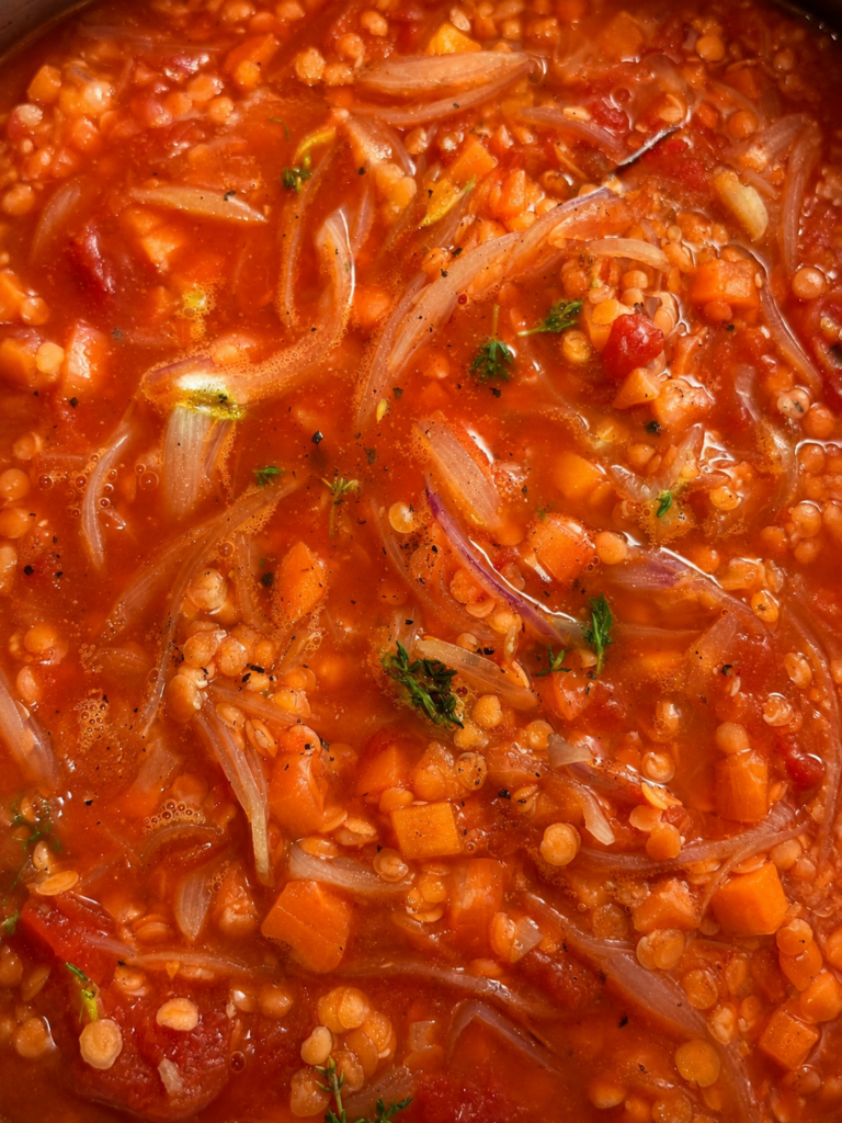 Close-up of French onion soup with lentils simmering with caramelized onions, red lentils, carrots, tomato and fresh thyme.